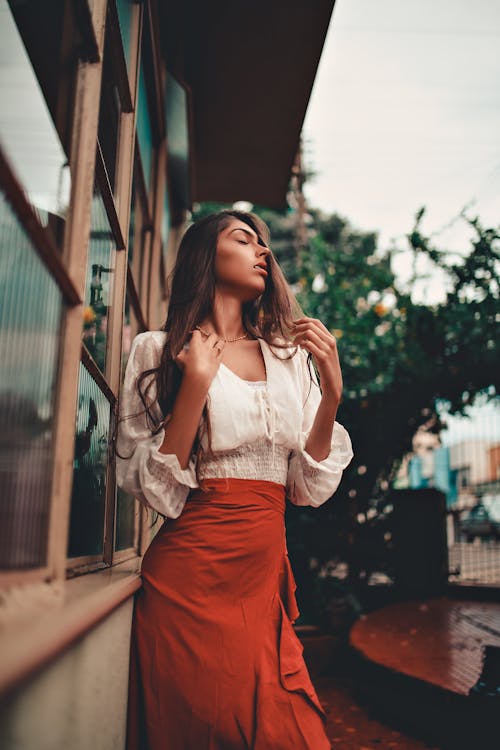 Woman in White Lace Long Sleeve Shirt and Red Skirt Standing on Sidewalk