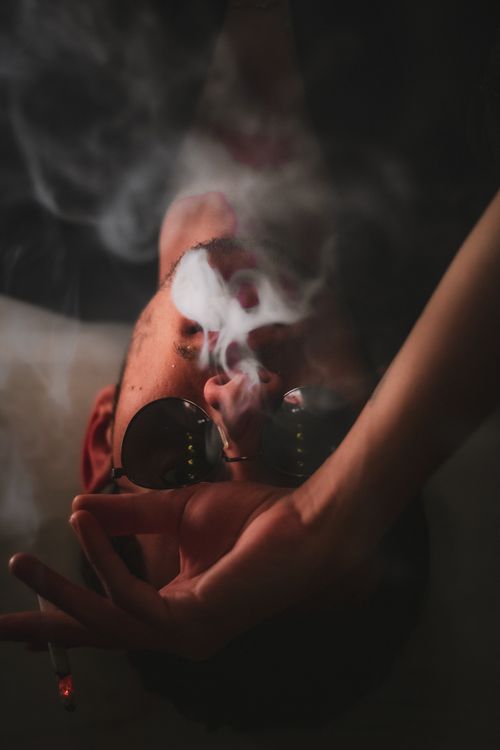 Free Artistic portrait of a person lying down with sunglasses and smoke for a moody effect. Stock Photo