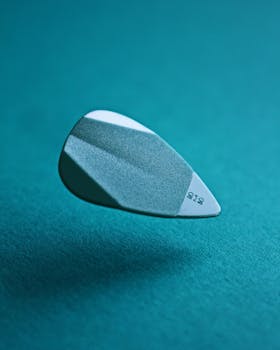 A detailed close-up of a levitating guitar pick against a teal background, showcasing texture.