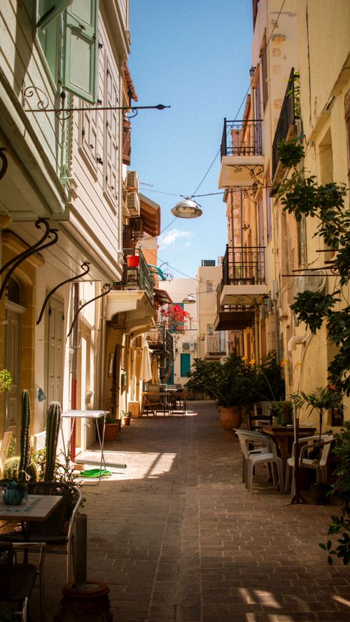 Gratis Un pittoresco vicolo a Chania, in Grecia, con edifici colorati e fiori vivaci. Foto a disposizione