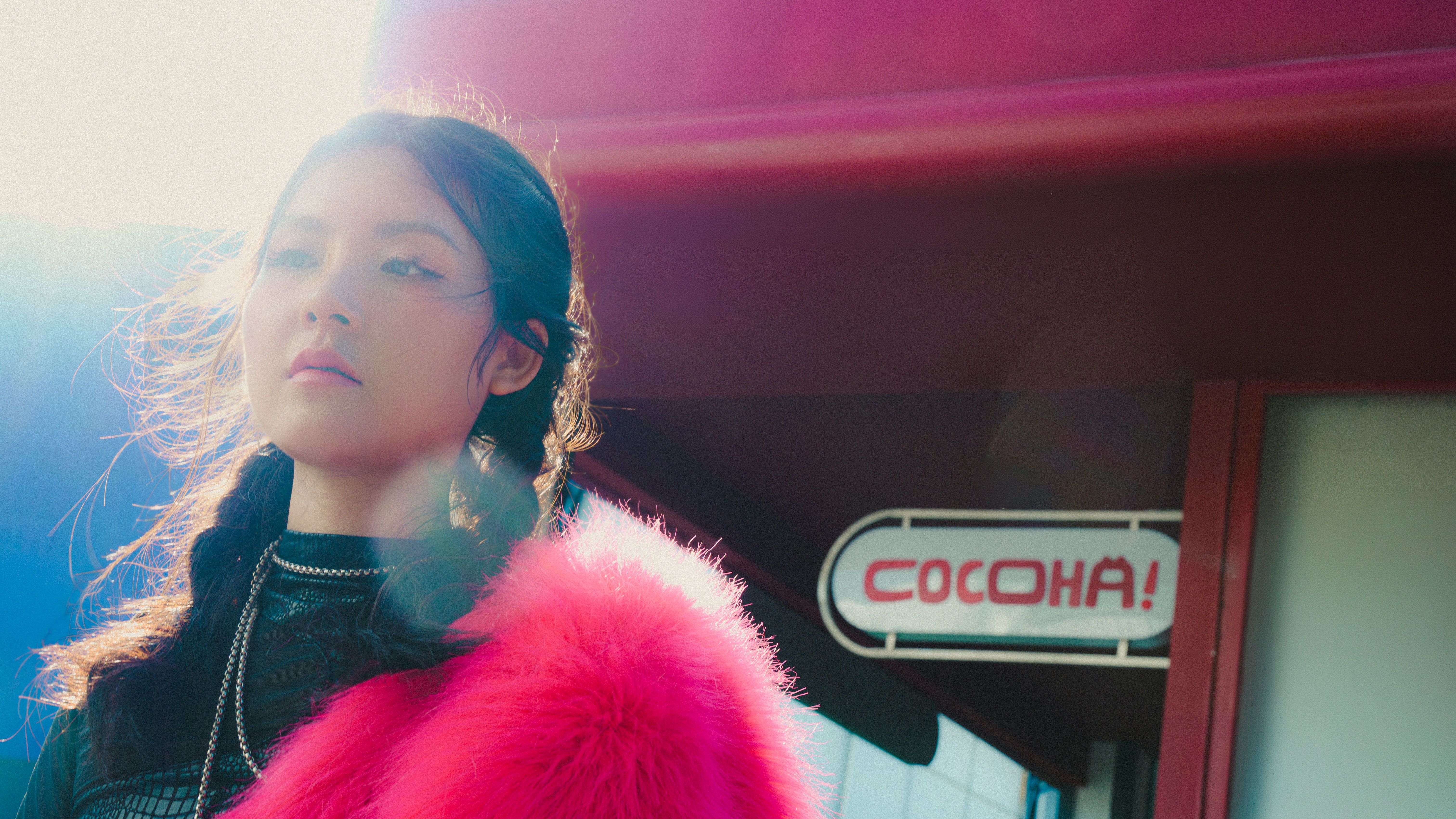 Stylish woman with pink fur outside a building labeled 'COCOHA!'