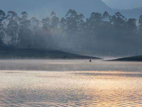 Serene misty morning view of Situ Cileunca lake with a lone fisherman in West Java, Indonesia.