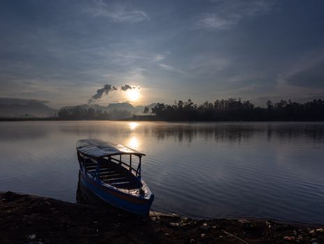 Tranquil morning view of a boat on Situ Cileunca Lake during sunrise in Pangalengan, West Java.