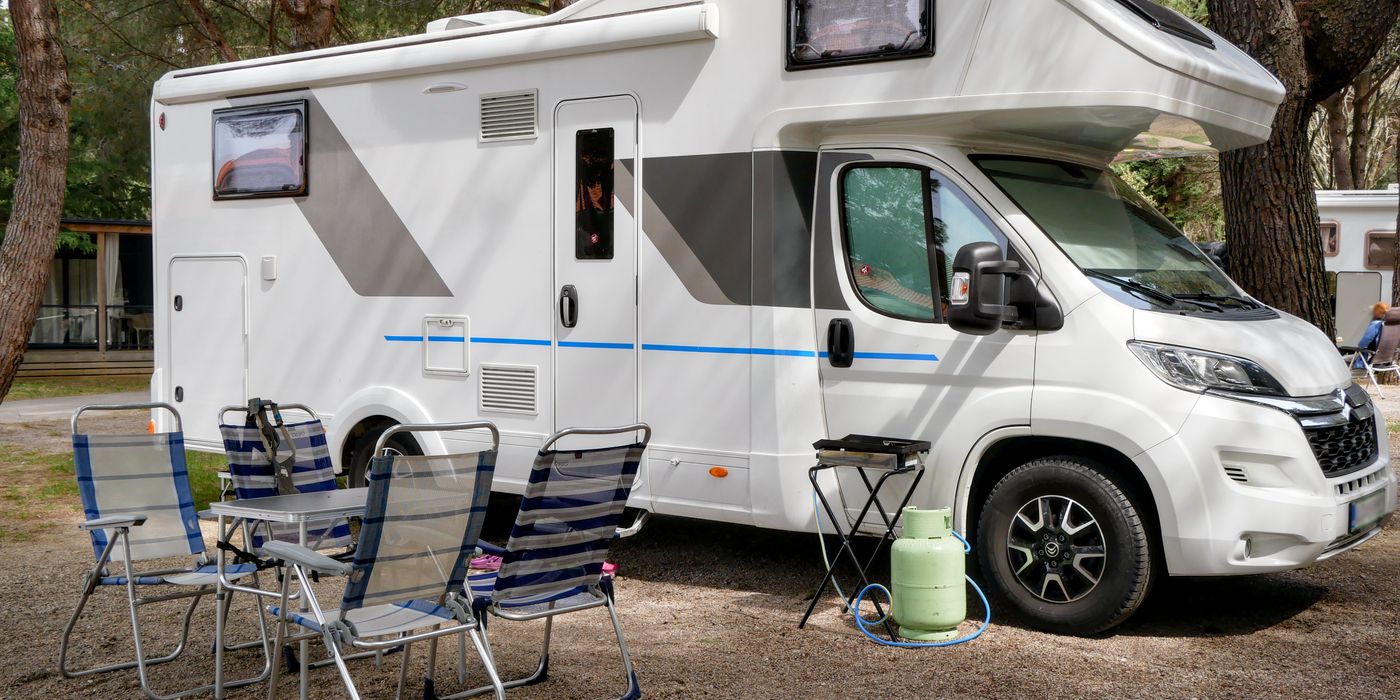 A motorhome set up at a forest campsite with chairs out