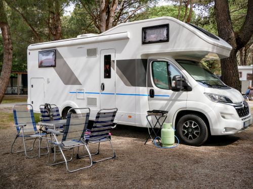 Free A modern RV parked in a forest campsite with outdoor seating, ideal for family adventures. Stock Photo