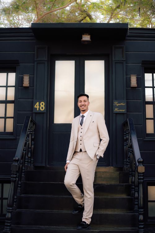 Free Man in a beige suit poses confidently on a classic black staircase outdoors. Stock Photo