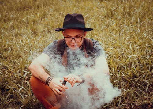 Man in Gray Shirt and Brown Cowboy Hat Sitting on Grass Field