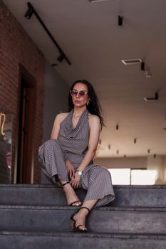 Fashionable woman in striped outfit and sunglasses posing confidently indoors.