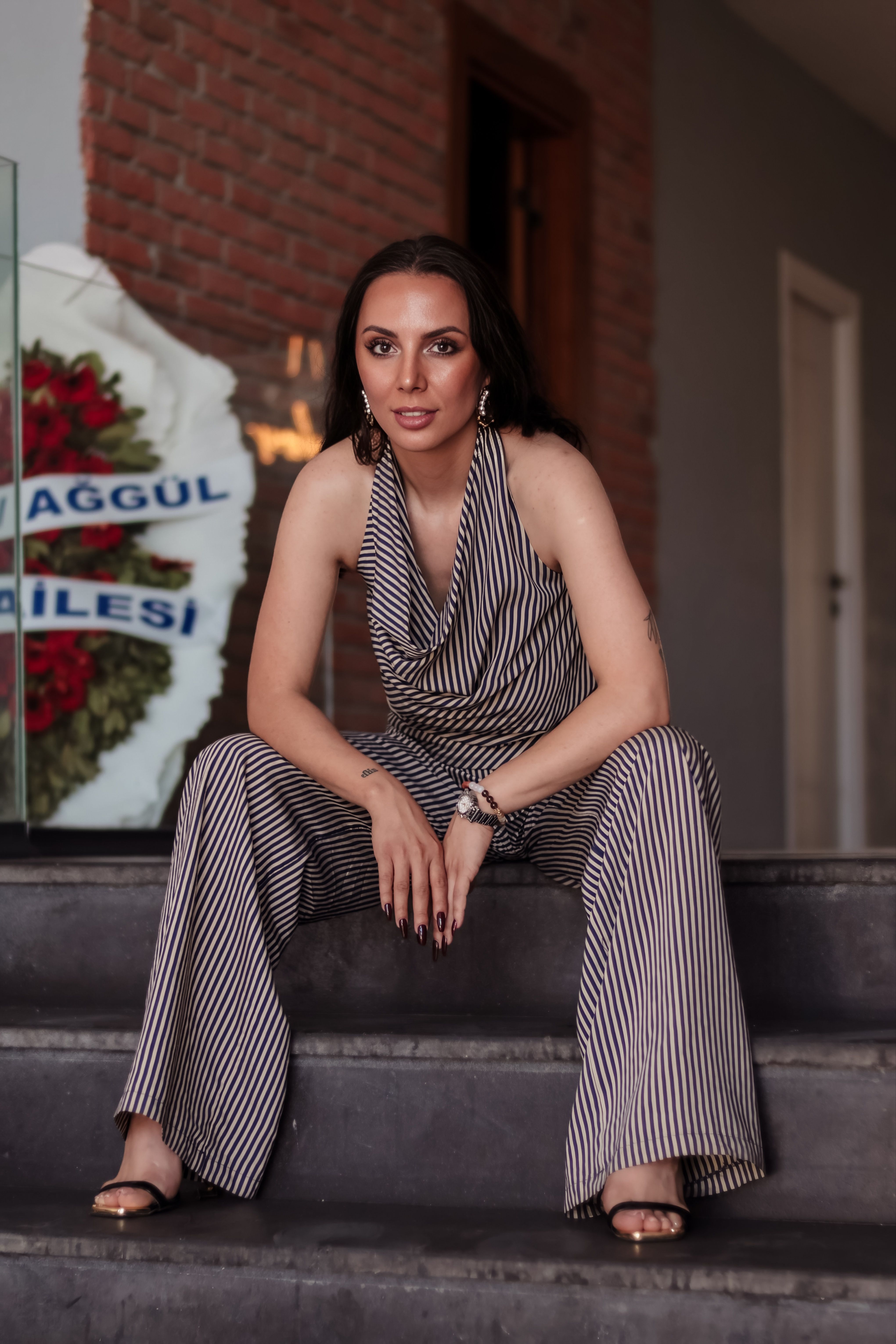 Confident woman in striped jumpsuit sitting indoors with a stylish look.