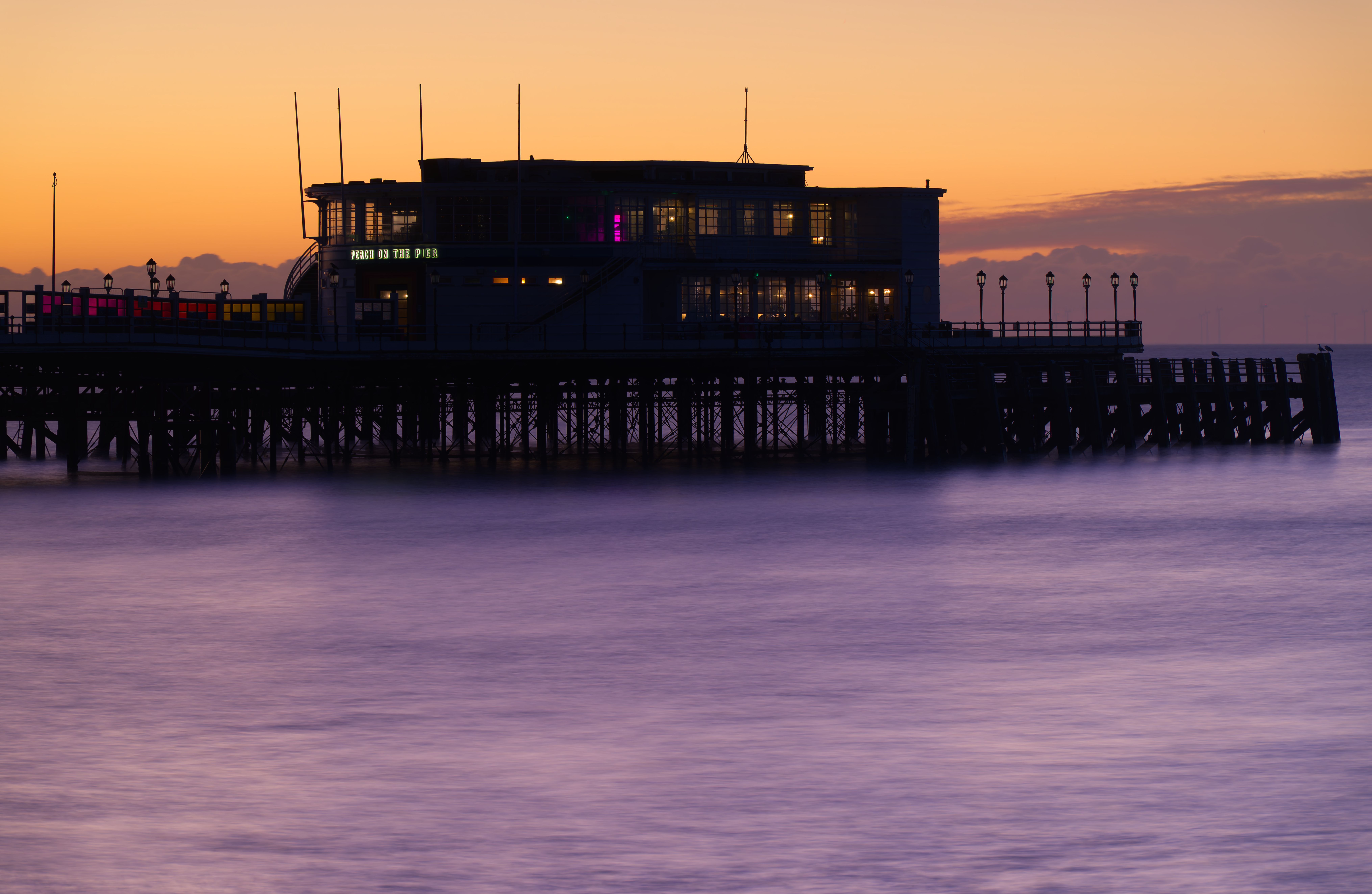 Tranquil sunset over the iconic Worthing Pier in England with a calm sea and vibrant sky.