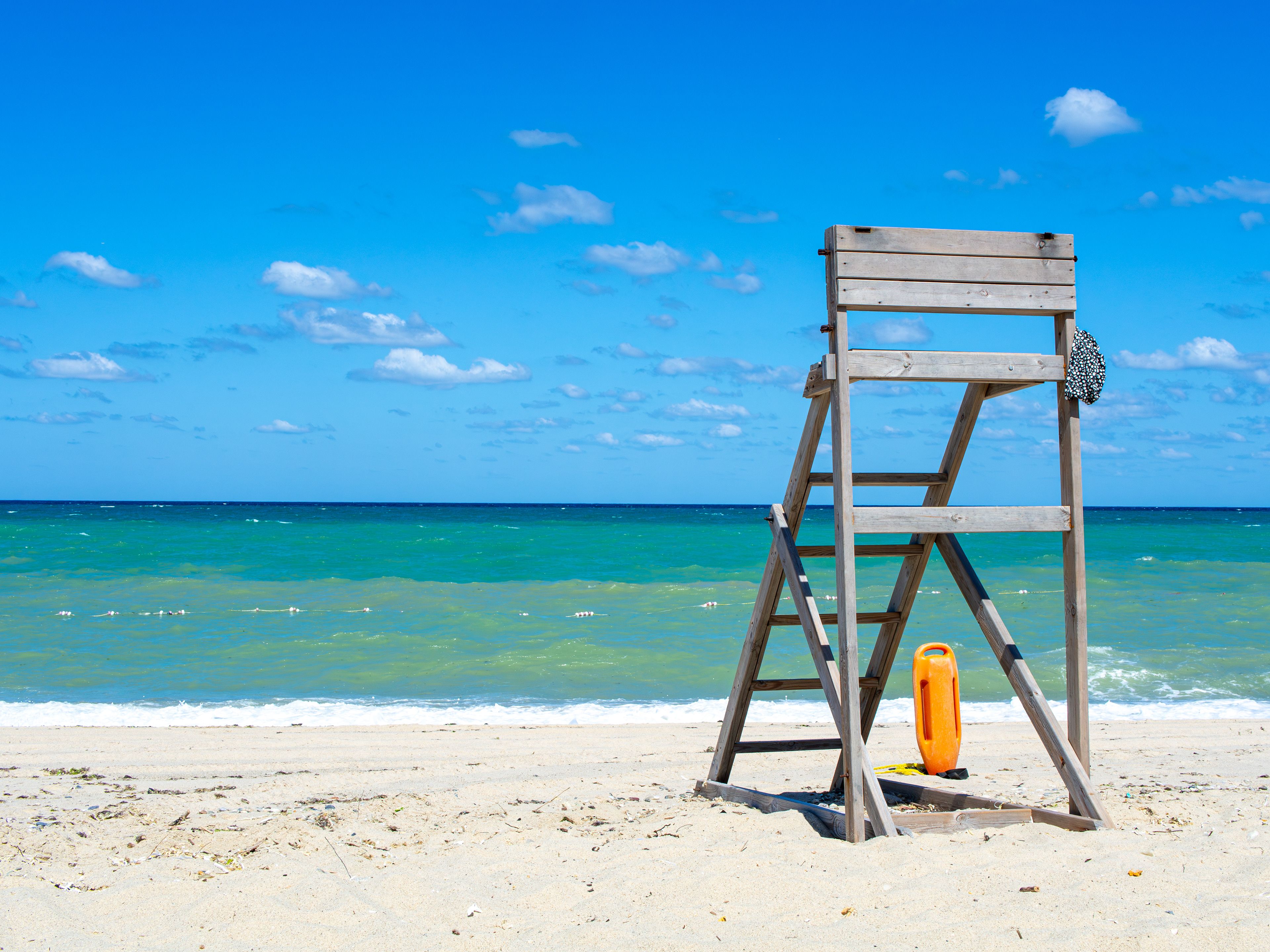 Empty lifeguard chair on a sunny beach with vibrant ocean views and clear skies.