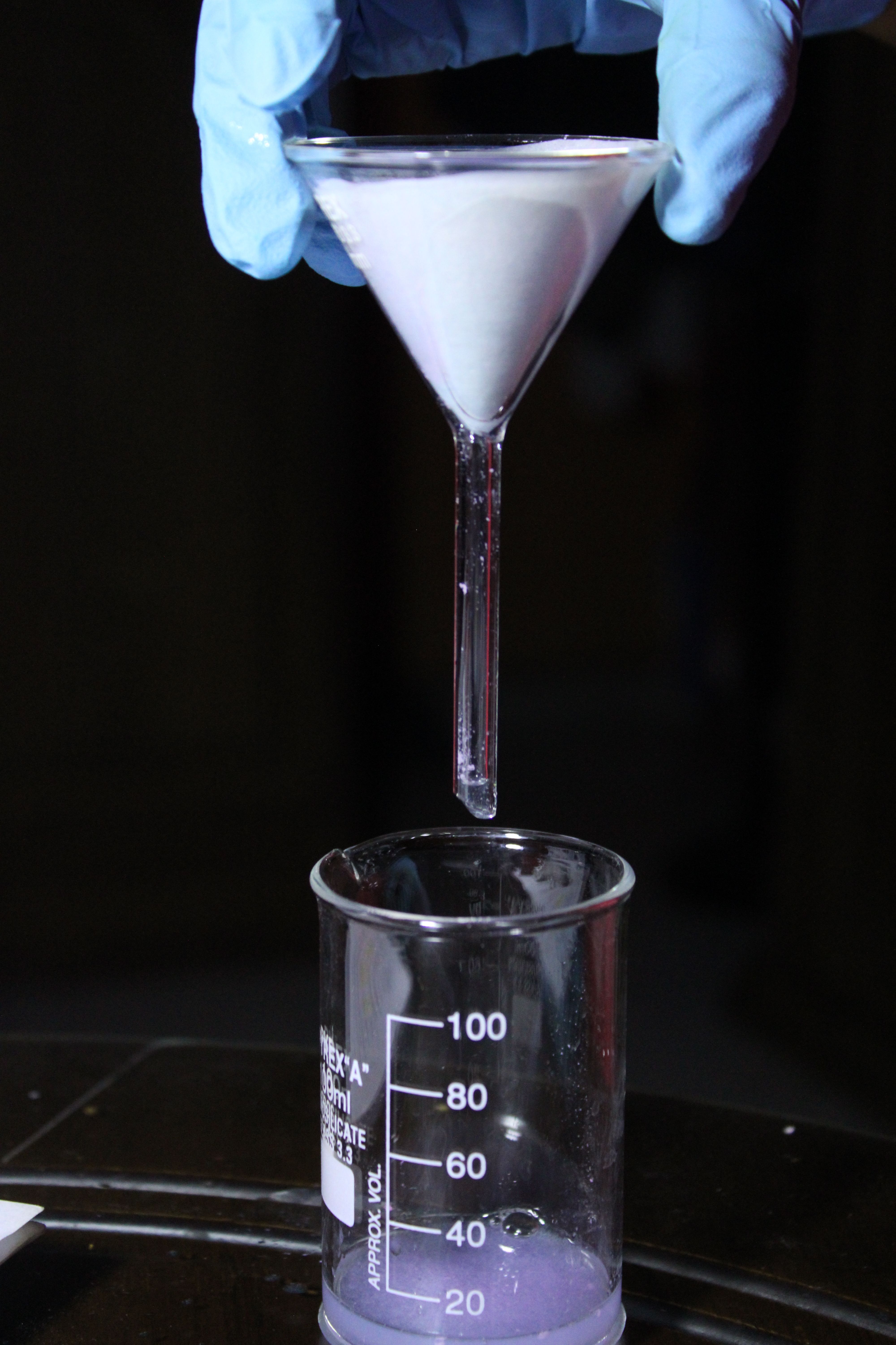 Scientist uses funnel to filter liquid into beaker in lab setting.