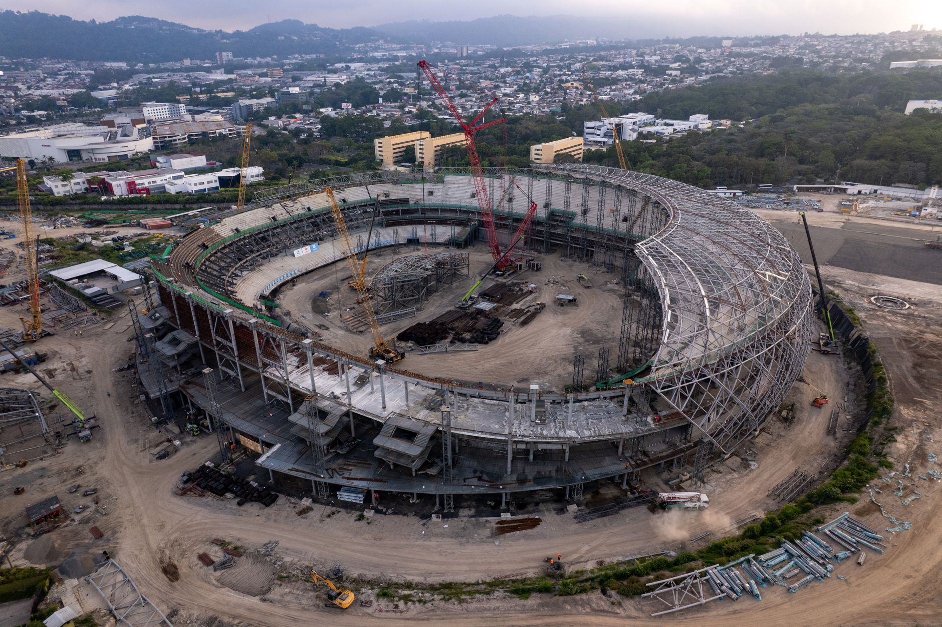 Aerial photograph of a large stadium under construction, showcasing structural progress and surroundings.