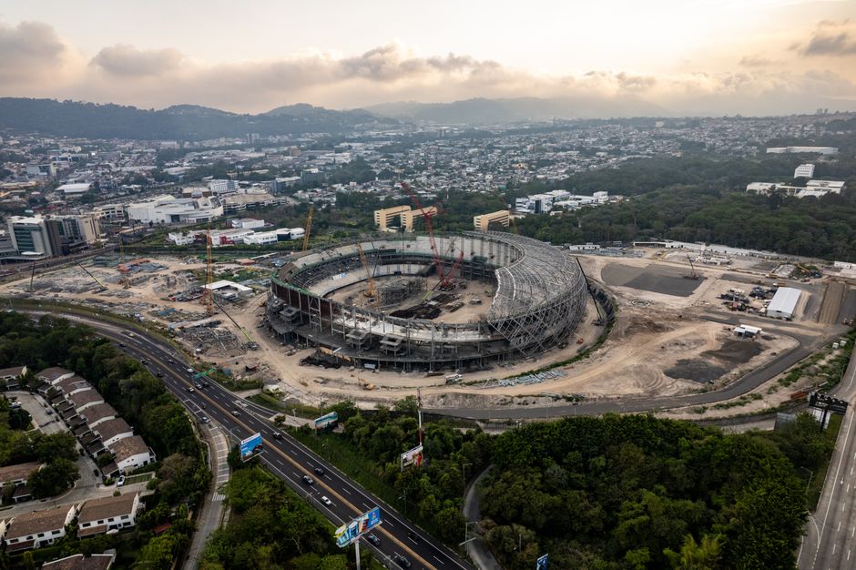Aerial view of a large stadium under construction in Tegucigalpa, Honduras, surrounded by cityscape and greenery.