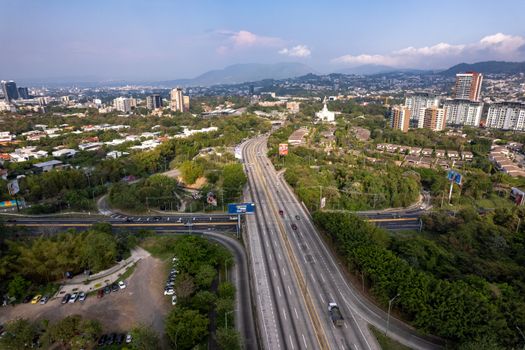 Aerial view of the bustling city of San Salvador with a busy highway and surrounding greenery.
