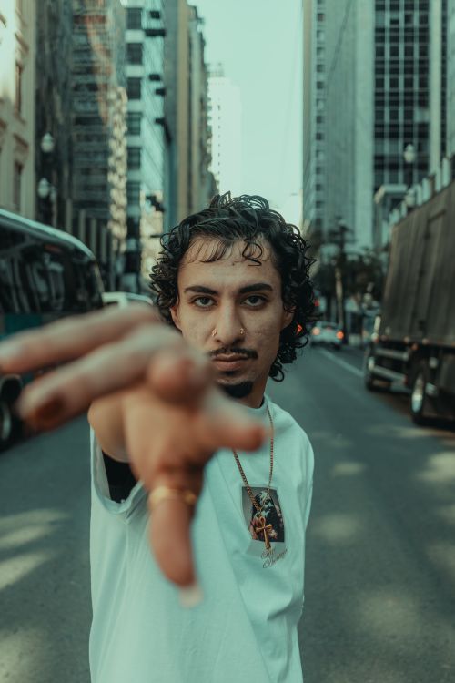 Free A man reaching towards the camera on a bustling city street lined with tall buildings. Stock Photo