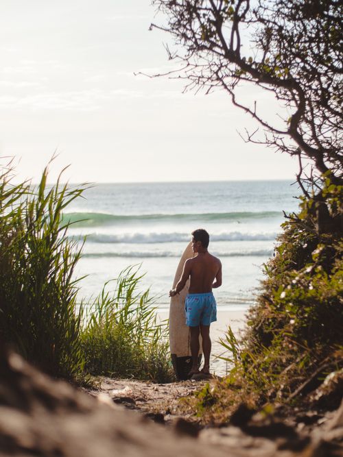 Free Shirtless surfer holding a surfboard, overlooking a tropical ocean at sunset. Stock Photo