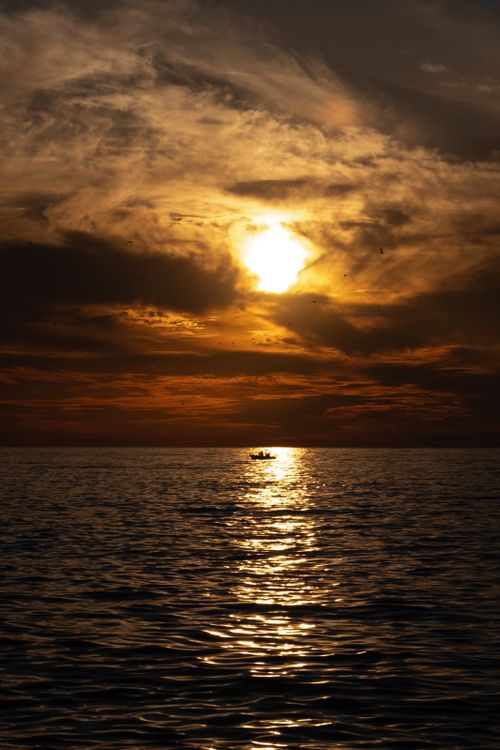 Free A tranquil sunset scene with a silhouette of a boat on the ocean, reflecting warm hues. Stock Photo