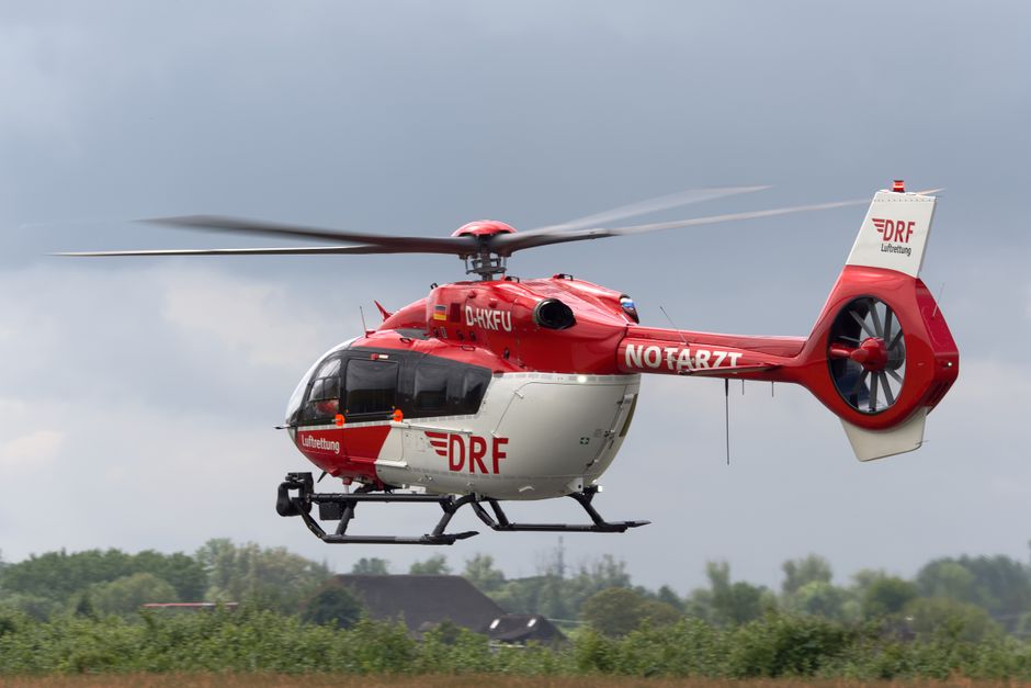 Red and white emergency medical helicopter flying outdoors against a cloudy sky.
