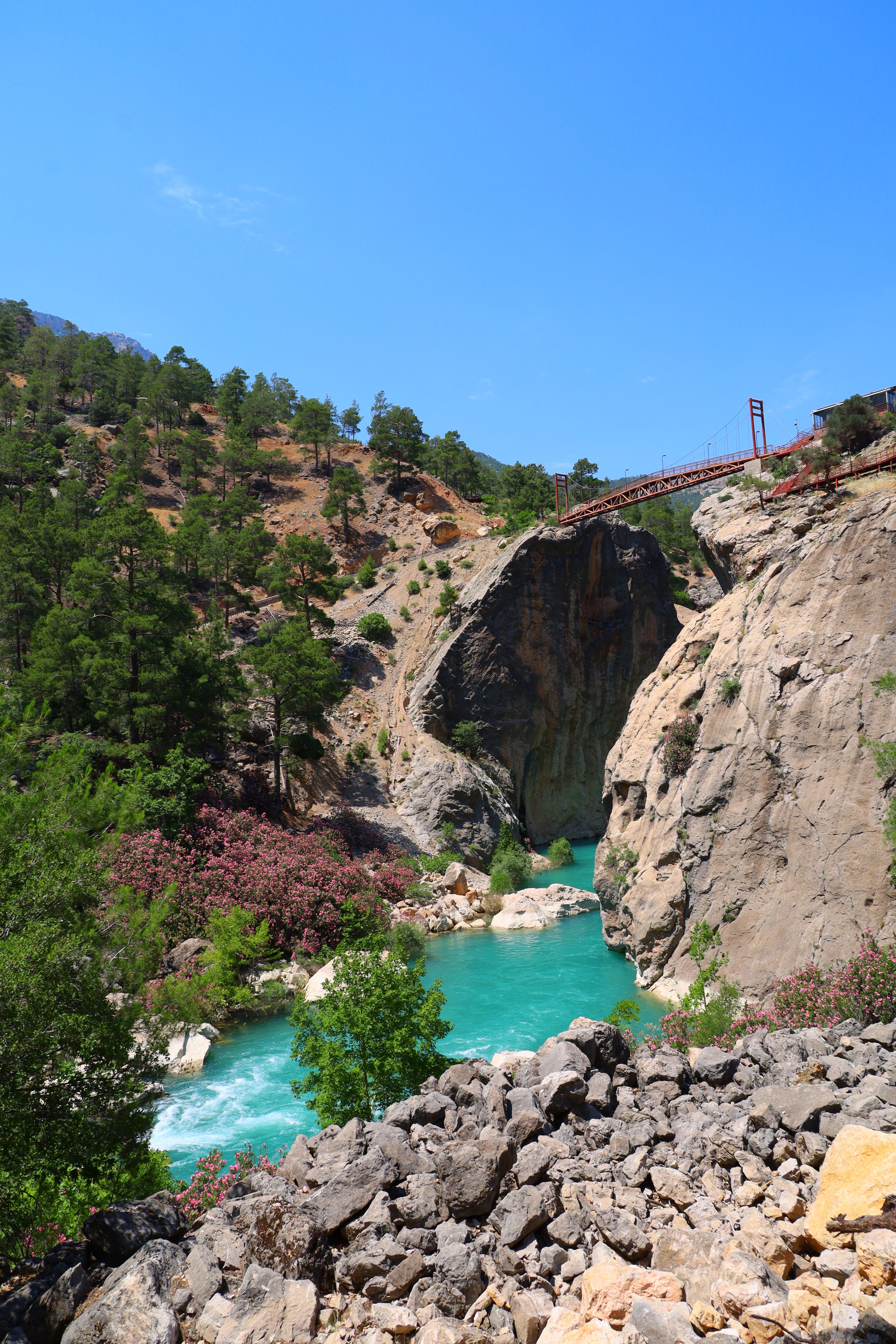 A beautiful gorge with a turquoise river and a bridge under a clear blue sky.