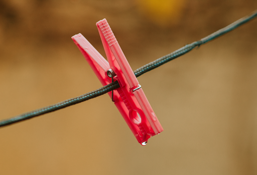 Close-up of a red clothespin on a wire with a water droplet, against a blurred background.
