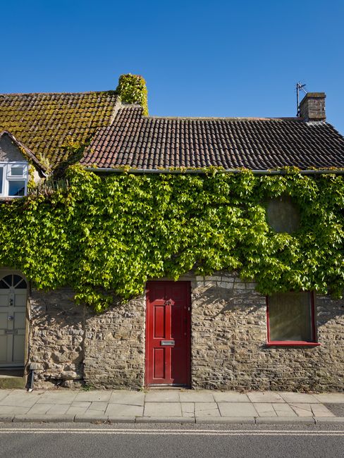 Picturesque stone cottage with ivy and red door under a clear blue sky in Malmesbury, England.