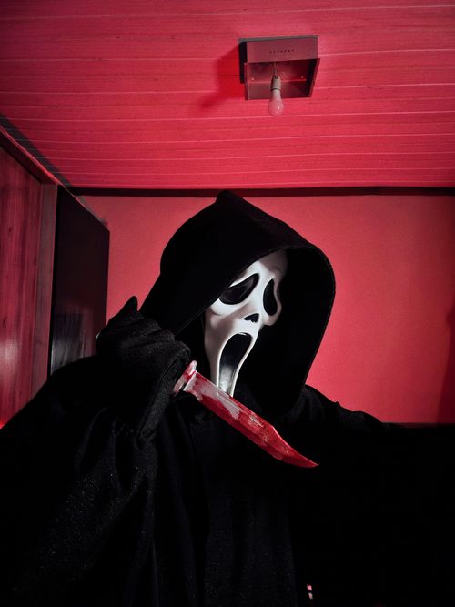 Free Masked horror figure holding bloody knife in eerie red-lit room. Stock Photo