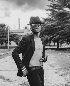 A fashionable man in a black hat poses confidently in an outdoor setting in Nigeria.
