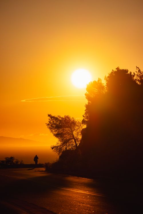 Free Dramatic sunset in Greece with silhouette of a lone figure on a road, captured in vivid warm tones. Stock Photo