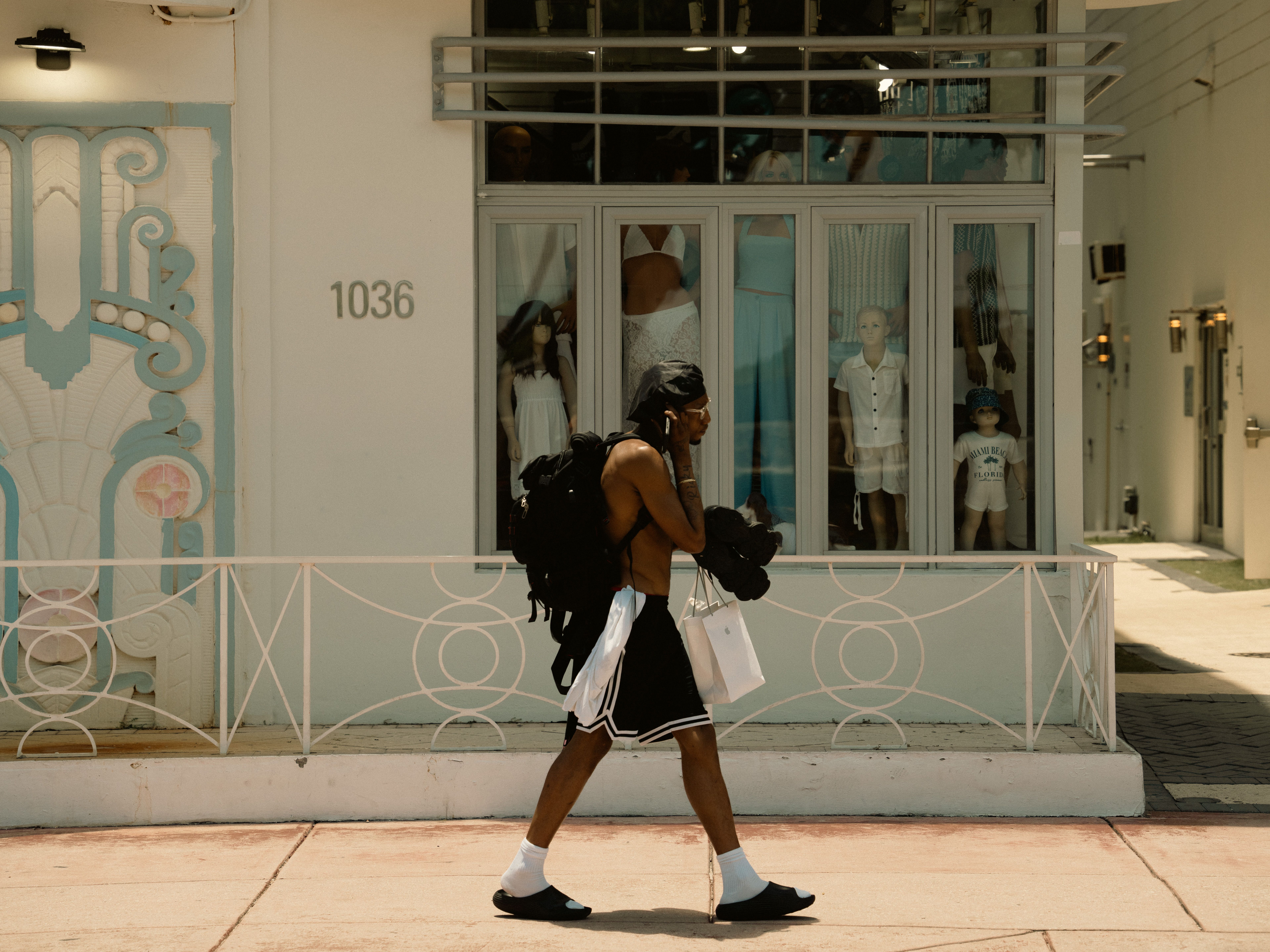 Man walking past a Miami boutique carrying shopping bags in the summer sun.