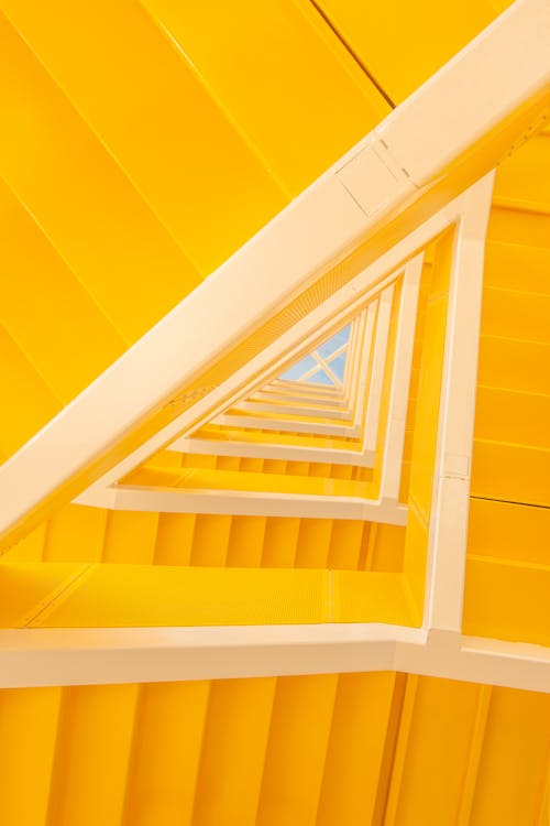 From below of modern geometric staircase made of yellow painted wooden panels inside modern house