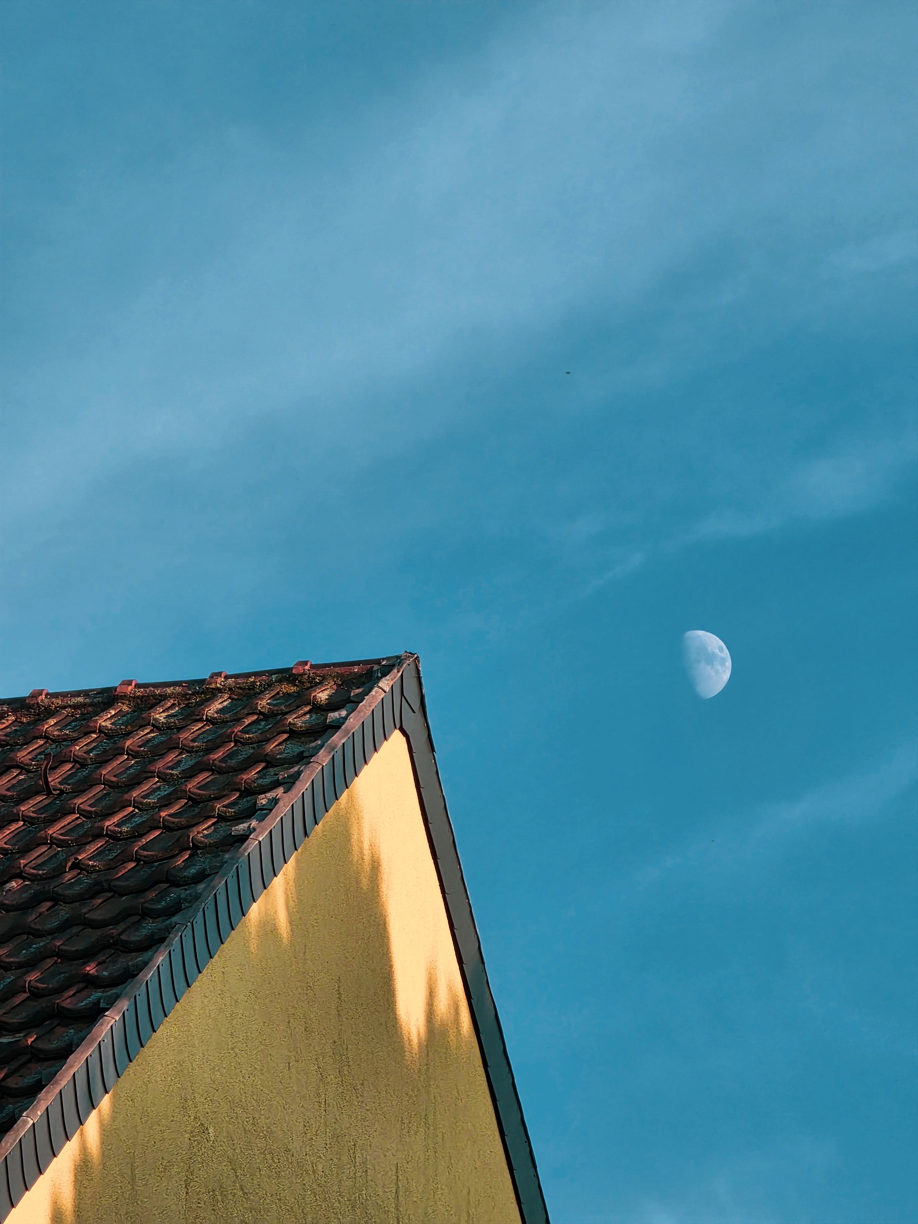 Yellow house roof against clear blue sky with visible moon.