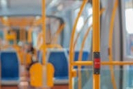 Red stop button on yellow handrail in modern empty public bus during daytime