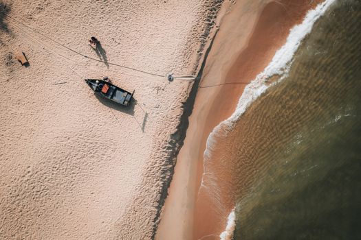 Aerial shot of a sandy beach featuring a small boat and gentle waves, captured on a sunny day.