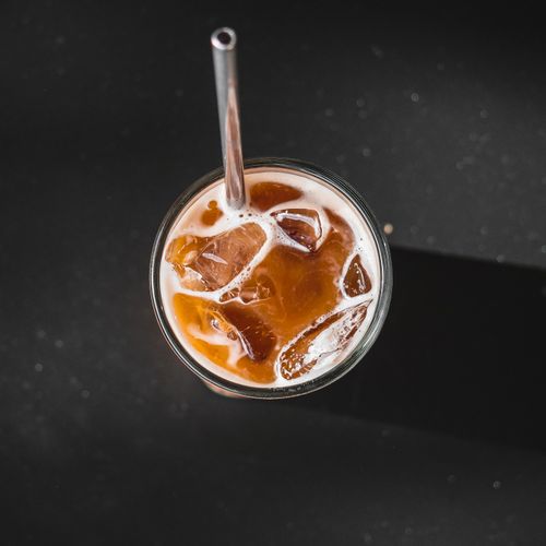 Free Top view of a glass filled with iced coffee and a metal straw, casting shadows on a dark background. Stock Photo
