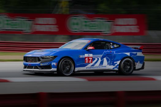 Blue Ford racing car speeding on a track in Lexington, Ohio, showcasing dynamic motion and automotive power.