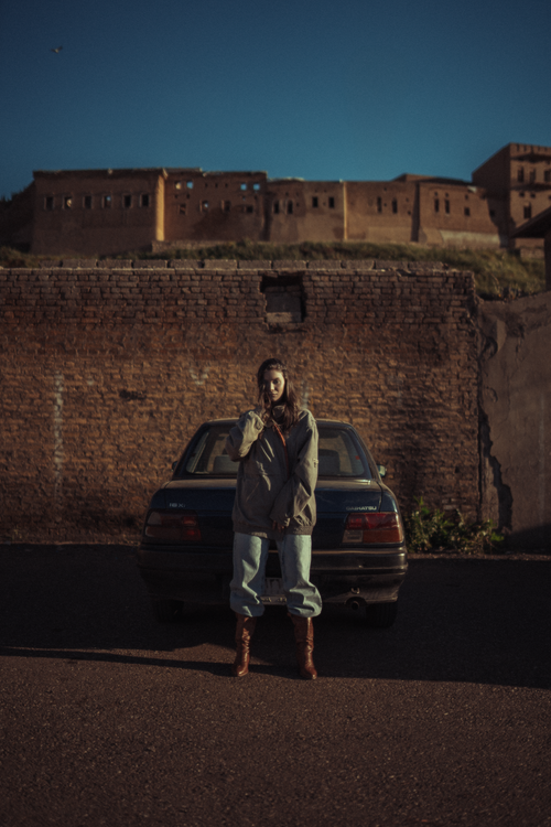 Free Portrait of a woman standing by a car near the historic Erbil Citadel in Iraq. Stock Photo