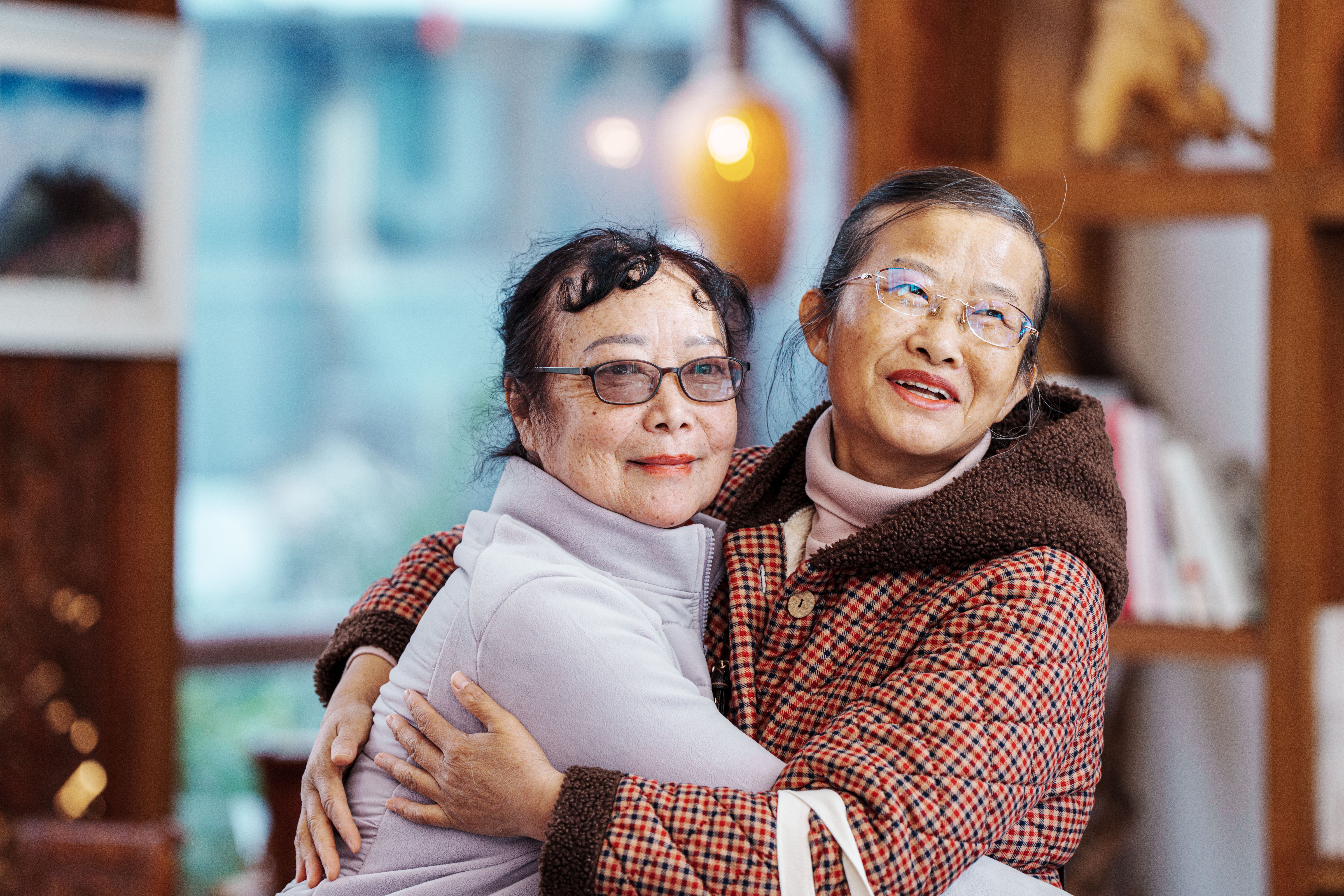 Two senior women embracing, expressing warmth and friendship indoors.
