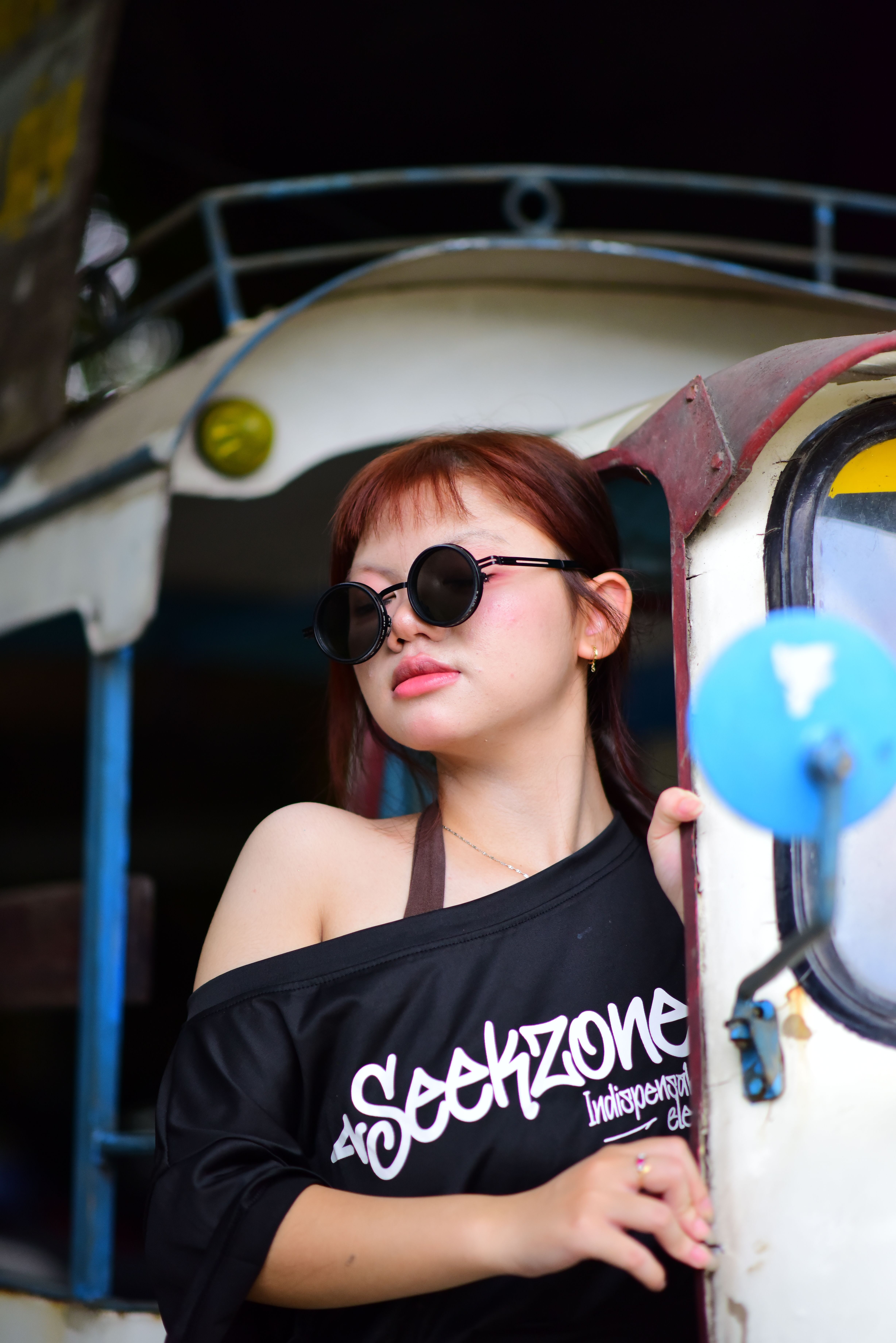 Young woman wearing sunglasses and a black top with Seekzone text, posing outdoors.