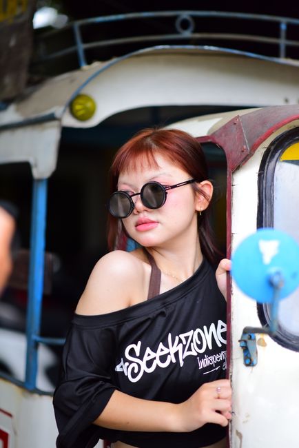 Stylish woman wearing sunglasses poses in front of a vintage tuk-tuk, embodying urban fashion.