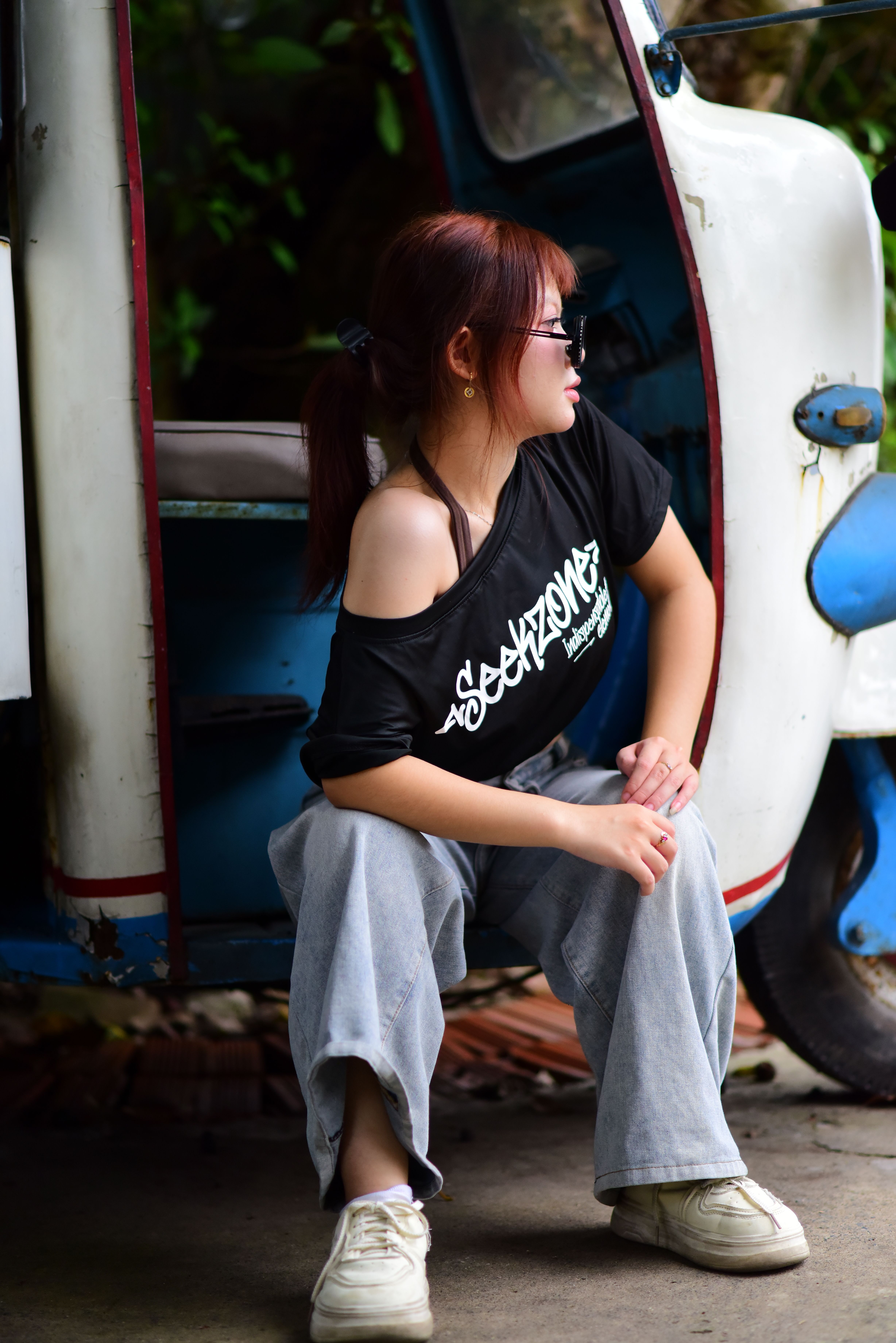 Stylish woman sitting by a vintage tuk-tuk, exuding casual elegance outdoors.