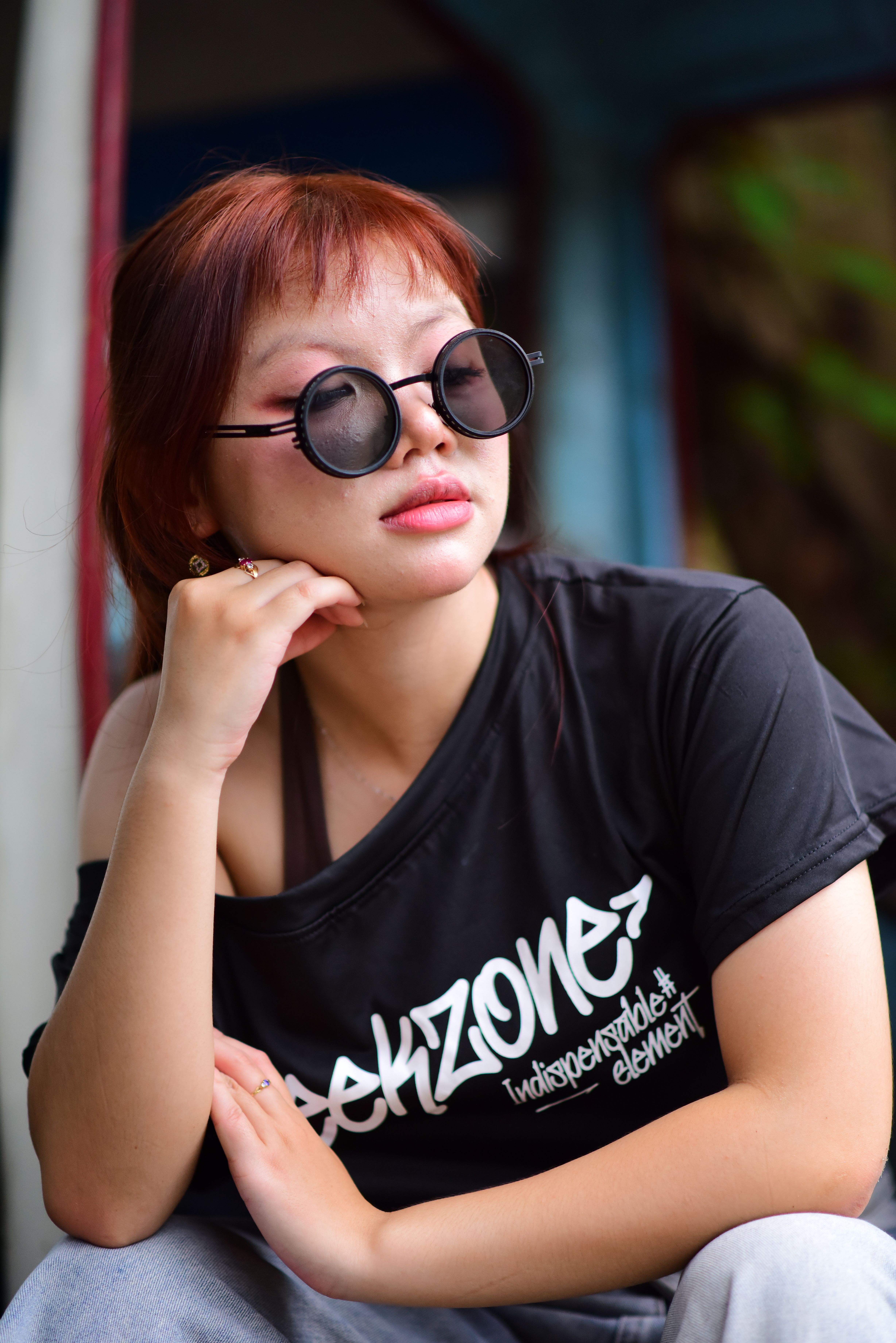 Stylish woman with round sunglasses and graphic tee sitting outdoors, exuding a cool vibe.