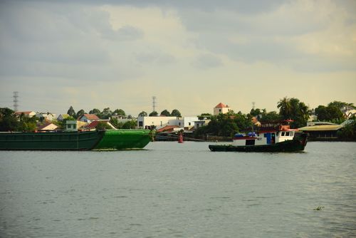 Free Calm river scene with fishing boats and a village backdrop under a cloudy sky. Stock Photo