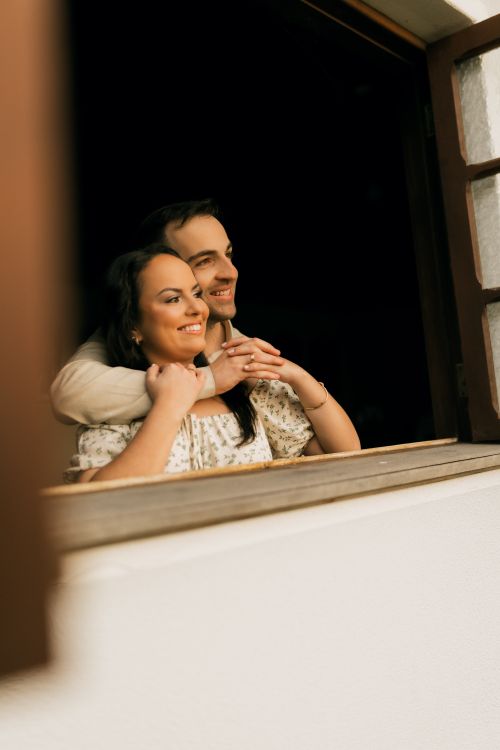 Free Happy couple enjoying a moment while looking out from an open window, smiling warmly. Stock Photo
