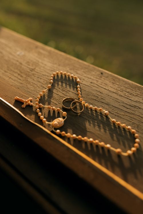 Free Serene composition of a rosary with wedding rings on wood, bathed in warm sunlight. Stock Photo
