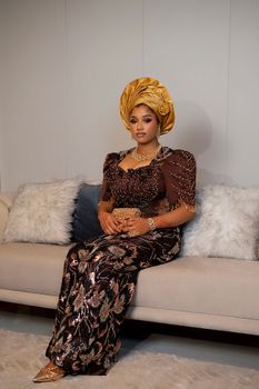 Portrait of a woman in traditional Nigerian attire seated indoors.