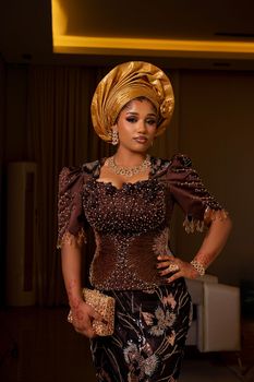 A beautiful Nigerian woman wearing traditional attire with intricate designs indoors.