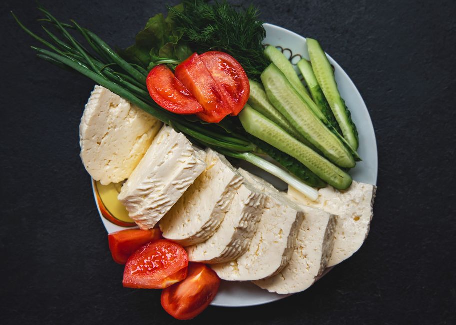 A vibrant plate of fresh cheese, tomatoes, cucumber, and herbs on a dark background.