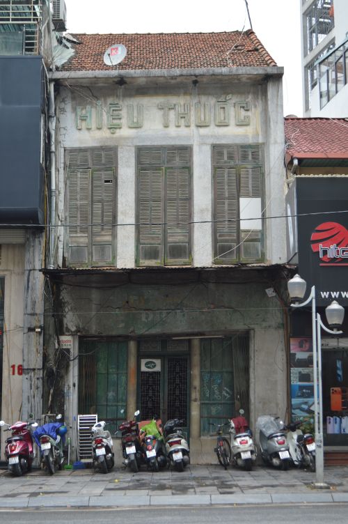Free An aged pharmacy building with motor scooters parked at the entrance, showcasing urban life. Stock Photo