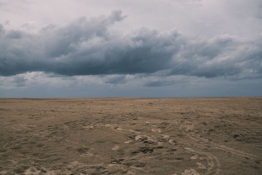 Empty beach with cloudy skies and dramatic clouds, creating a moody atmosphere.
